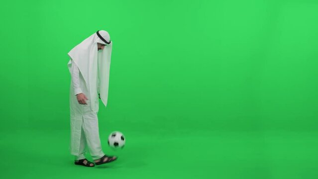 An Arab man in a white robe on the background of a green background, plays with a soccer ball, kicks the ball with his foot, chromakey template.