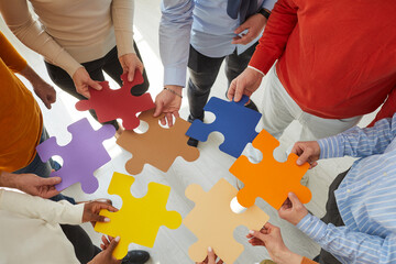 Close up top view of diverse multiracial businesspeople hold jigsaw pieces connect puzzle seek for business solution in office. Employees or colleagues involved in teambuilding activity or training.