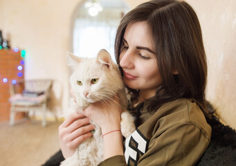 Cute smiling girl holding a cat in her arms at home. The concept of pets, friendship, trust, love and lifestyle, pet care.
