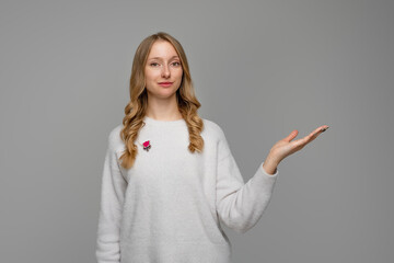 Portrait of happy blonde young woman, pointing hand right and showing at promo offer, advertisement, stands in white sweater against gray background