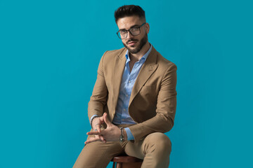 bearded young man in beige suit holding hands and sitting