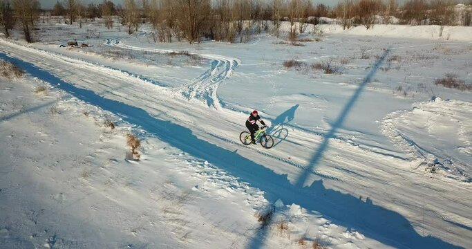 A man in a jacket and a cap rides a bicycle on a winter day. Snowy road, sunny.