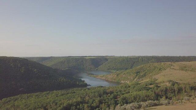 The drone flies over the river. Around the river canyon, which is covered with grass and trees. Morning sun. Dawn. Summer. Gray blue sky. There are no people in the video. Reserve.