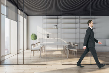 Businessman walking in modern conference room interior with window and city view, glass partition, wooden flooring and daylight. Workplace concept.