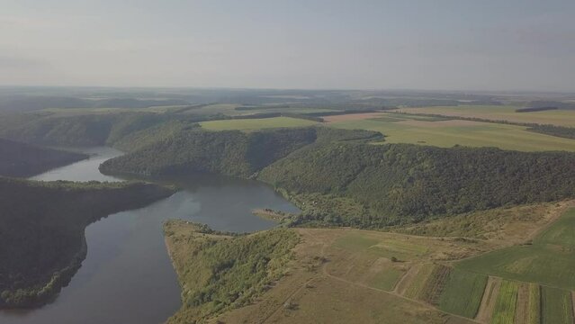 The drone flies over the river. Around the river canyon, which is covered with grass and trees. Morning sun. Dawn. Summer. Gray blue sky. There are no people in the video. Reserve.