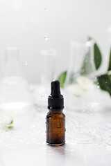 Glass dropper bottle with essential oil on wet table under falling down drops