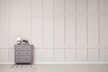 Grey chest of drawers near empty molding wall indoors, space for text