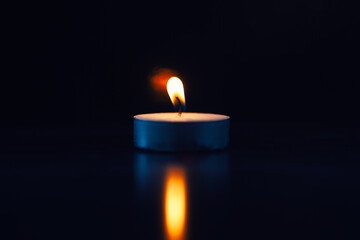 Burning candle with fading flame with reflex, black background