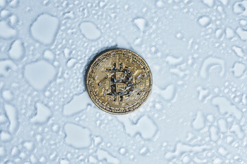 Bitcoin coin thawed from ice in drops water on light background.