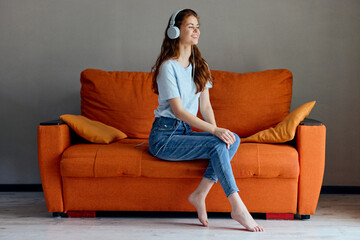 beautiful woman on the orange sofa listening to music with headphones technologies