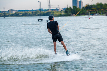 Rear view of wakeboarder sliding on water of city river holding on to towing rope