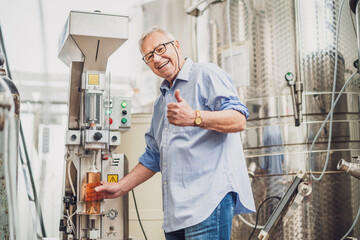 Senior man is using machine to cork wine bottle in his distillery.