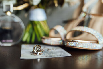 beautiful gold wedding rings on wooden table next to bouquet and shoes
