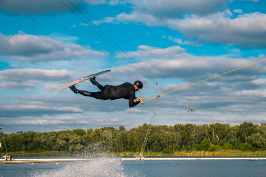 Athletic man practicing wakeboard tricks in training wake park on summer day