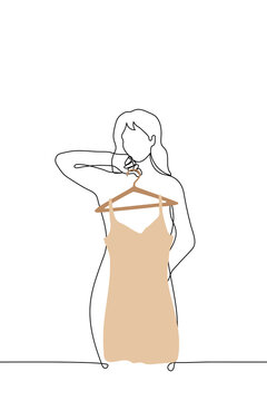 woman stands in front of mirror and leans against hanger with short beige dress with spaghetti straps - one line drawing vector. concept of trying on new dress