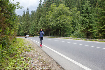 Runner woman running on the mountain road through the forest. Female sport girl training outdoors for marathon