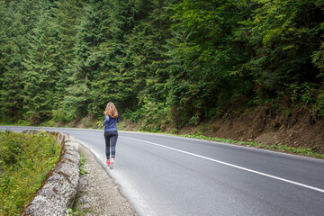 Young fitness woman running on the road through the forest. Slim girl jogging in the morning along the road.