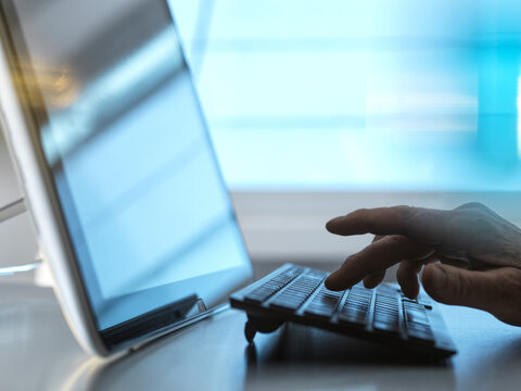 Hand of engineer typing on keyboard by tablet PC at desk in home office