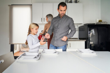 Family consisting of father, mother and daughter setting the table to eat in the kitchen.