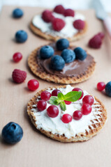 Waffles with cream cheese and chocolate, mint, cranberries, raspberries and blueberries on a wooden board. Romantic breakfast with teapot, cup of tea, knife, fruits on waffles