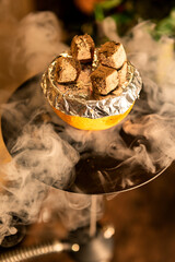 Hot coals on a hookah bowl with a dark background and smoke. Stylish oriental hookah.