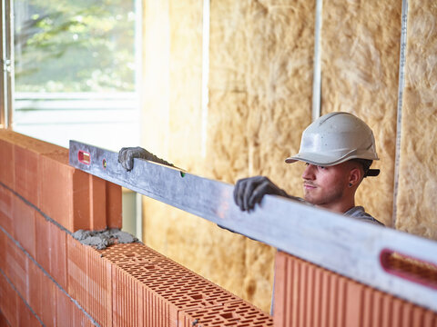Concentrated bricklayer using spirit level to measure bricks at construction site