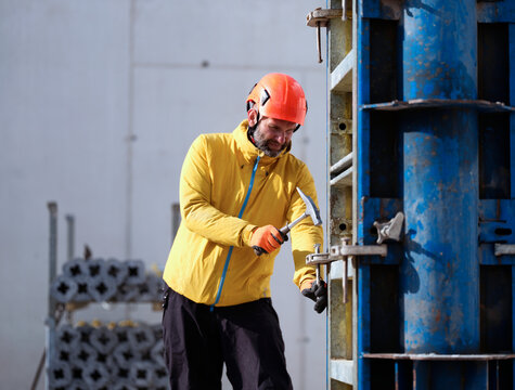 Worker fastening nail with hammer on metal structure at construction site