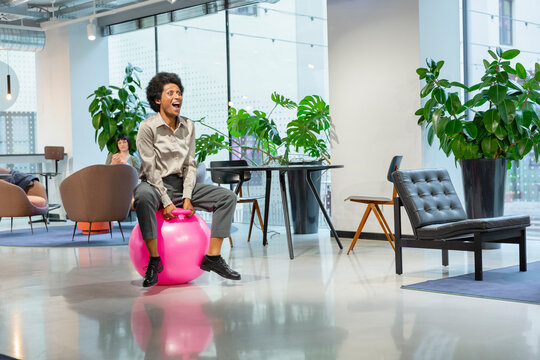 Cheerful businesswoman sitting on hopper ball in lobby