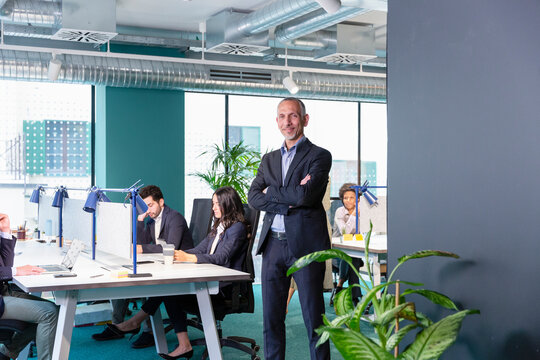 Confident manager with arms crossed and colleagues working in background at office