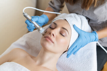 Obraz na płótnie Canvas Young woman lying on cosmetologist's table during rejuvenation procedure. Cosmetologist take care about neck and face skin youthfull and wellness. Hardware face cleaning procedure