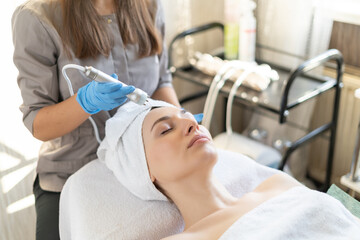 Young woman lying on cosmetologist's table during rejuvenation procedure. Cosmetologist take care about neck and face skin youthfull and wellness. Hardware face cleaning procedure