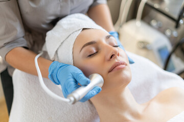 Young woman lying on cosmetologist's table during rejuvenation procedure. Cosmetologist take care...