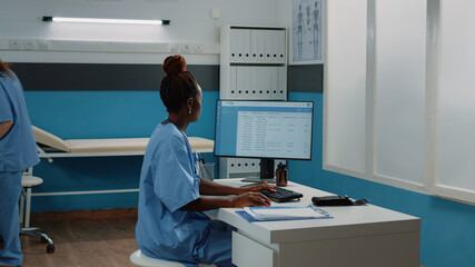 Medical assistant typing on computer keyboard in cabinet. Woman working as nurse with uniform using monitor for checkup appointments and healthcare practice while sitting as desk.