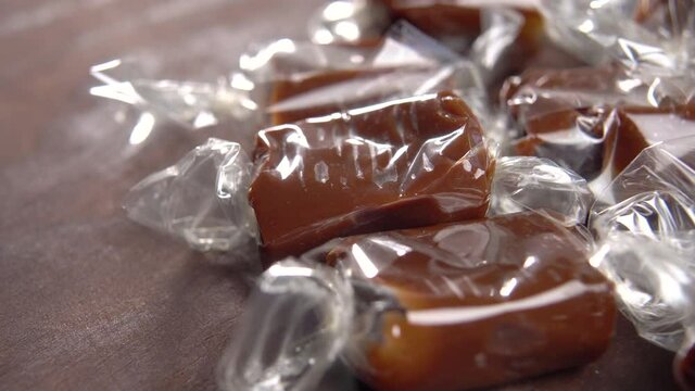 Brown candy toffees in a wrapper on a wooden rustic background. Sweet xmas taffy. Macro. Rotation. Chocolate creamy caramel