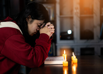 Christian female while praying and worship for Jesus with candle stick in low light. christian people praying while hands worship over a Bible. learning religion. Selective focus on hands.