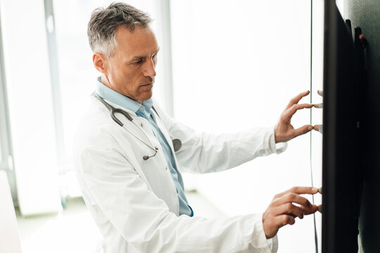 Mature Doctor Using Touch Screen Computer Monitor In Hospital