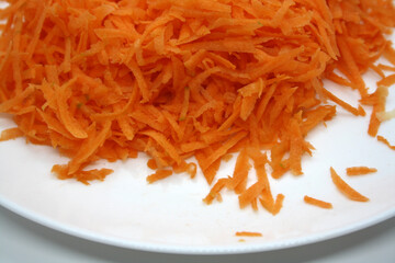 Grated orange carrots on a white plate. Background.