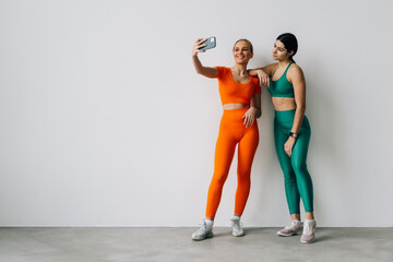 Portrait of young two smiling sporty women taking a selfie photo in the gym.