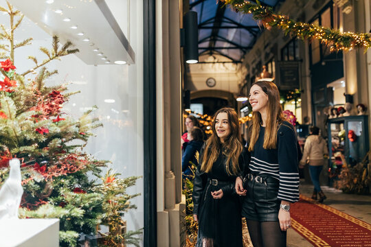 Cheerful friends looking at Christmas tree through store window at night