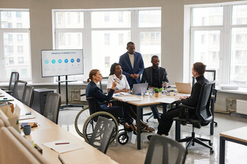 Diverse group of business people at meeting table in office with woman using wheelchair in...