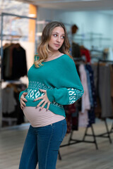 Pregnant blonde young woman trying on clothes in a clothing store