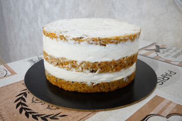 Carrot cake with orange curd. Three-tiered cake with white cream. Cake on a light beige background with a pattern, on a dark round substrate.