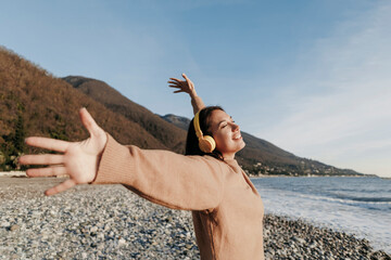 Smiling young woman listening music through headphones dancing at beach