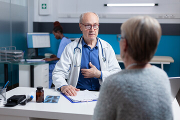 Obraz premium Medic attending consultation appointment with old woman in cabinet. Healthcare specialist and woman having conversation about disease diagnosis at annual checkup visit. Medical exam