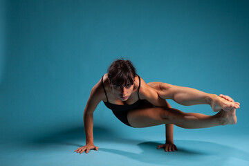 Fototapeta na wymiar Active fit person standing in hands working at arm balance in studio with blue background. Personal trainer practicing gym exercices stretching body muscles during sport workout