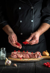 Cook prepares meat for roasting in the restaurant kitchen. The chef puts spices and red viburnum on fillet.
