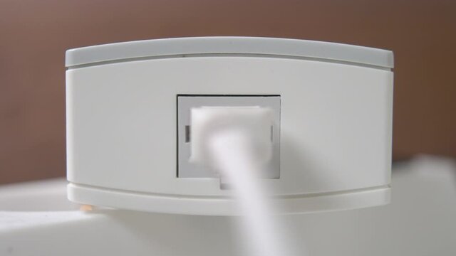 Connecting network internet plug in a white wireless modem on a brown background. Plugging ethernet cable to a router. Close up