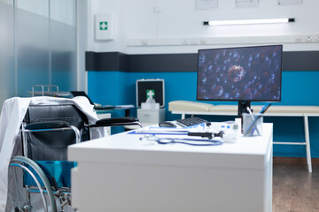 Empty examination office with computer standing on desk table having cornavirus illustration on screen during covid19 global pandemic. Hospital room equipped with professional tools. Virus image