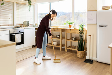 Young woman cleaning kitchen floor with broom at home