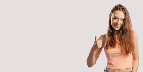 Fototapeta na wymiar Beautiful young girl smiling and shows thumbs up gesture hand on a white isolated background. Positive woman points to an idea, a place for advertising
